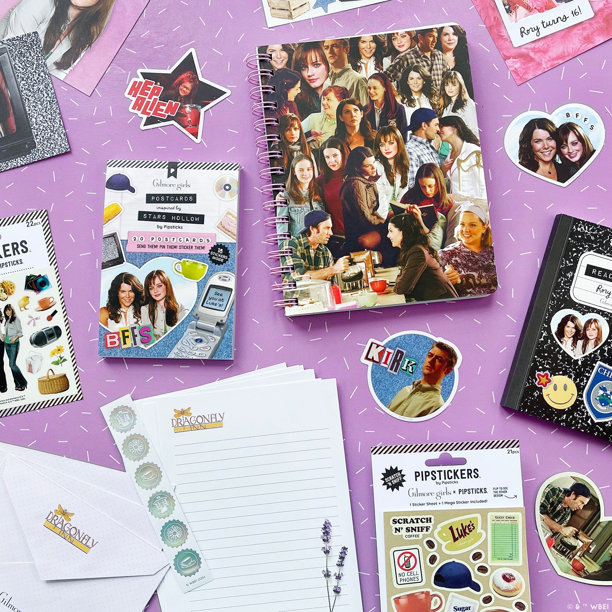 A styled flat-lay of Gilmore Girls stationery and stickers on a purple background. The set includes a spiral notebook with a collage of young women, a pack stickers, a notepad, and other matching stationery items.