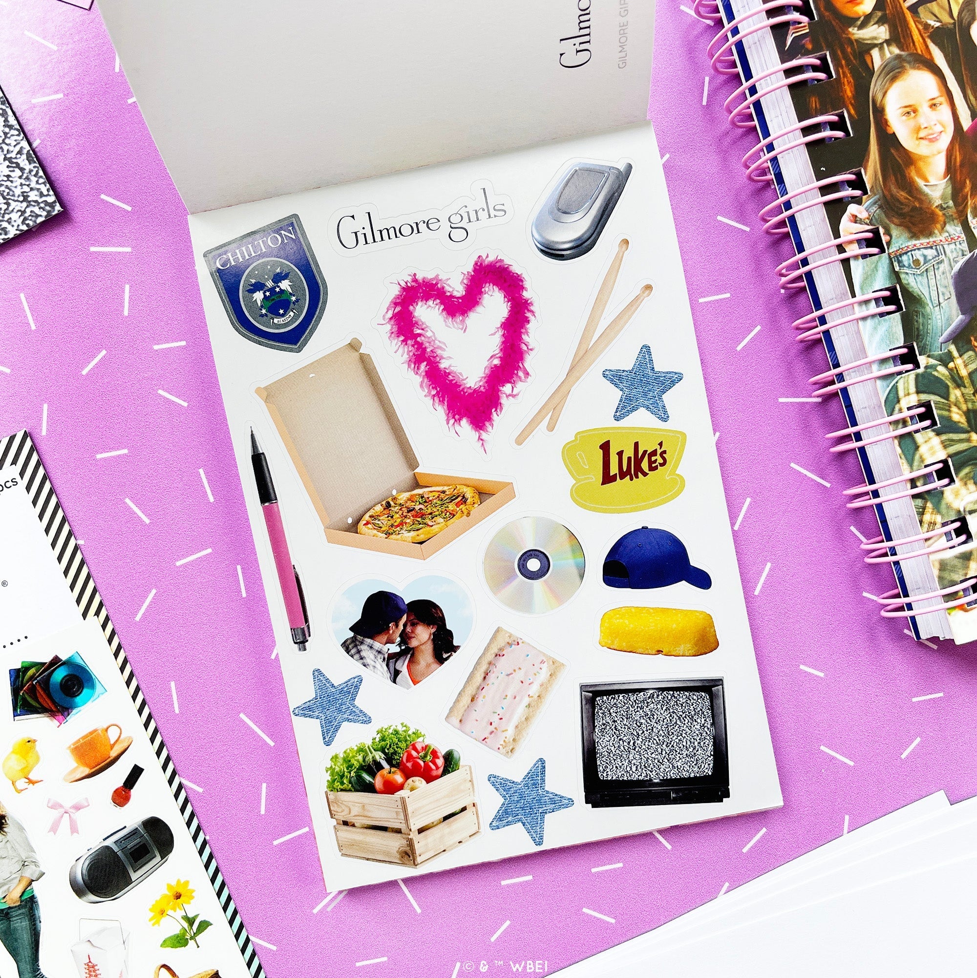 A sheet of photo stickers displayed on a purple background, surrounded by other stationery items like a spiral notebook and a pen. The stickers feature various pop-culture references and text such as 'Gilmore girls', 'Luke's', and 'Chilton'.