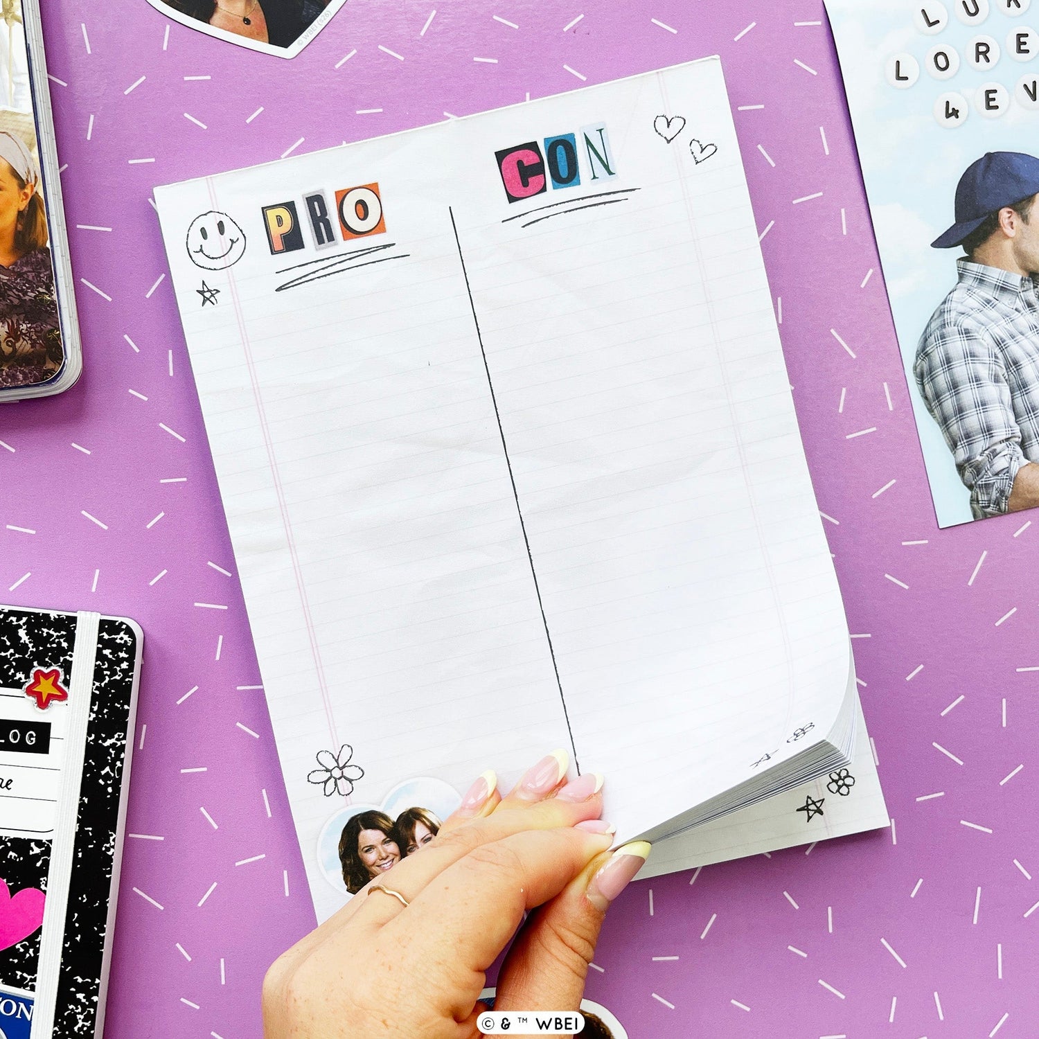 A hand holds a stack of white lined notepad sheets with colorful decorative headers reading 'PRO' and 'CON' on a purple background with scattered doodles and stationery props.