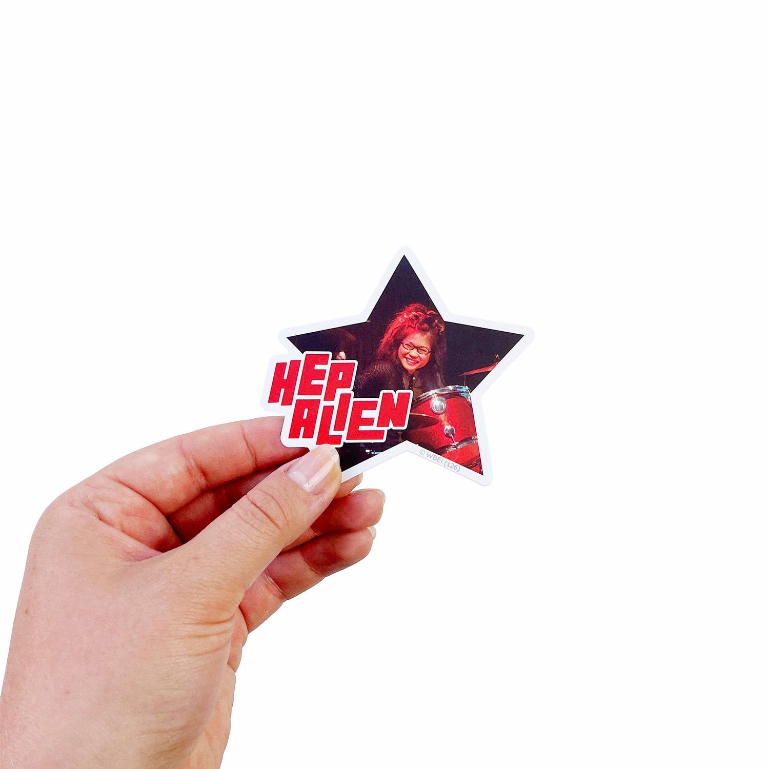 A hand holding a star-shaped sticker featuring a photo of a woman in a red outfit with the text 'HEP ALien' in red and white, against a plain white background.