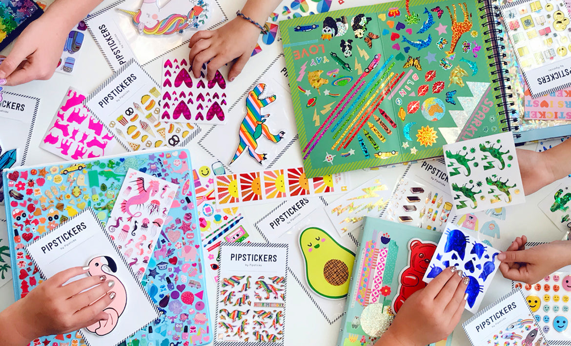 Several children's hands spreading Pipsticks sticker sheets across a table and filling a sticker book